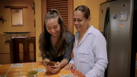 Mother and teenager daughter looking at a cell phone together and laughing Stock Footage