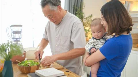 Mother and tiny child in the kitchen preparing dinner with grandfather Mot... 스톡 사진