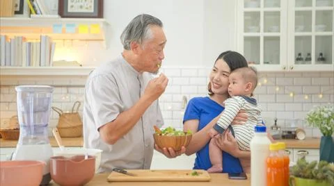 Mother and tiny child in the kitchen preparing dinner with grandfather Mot... Stock Photos