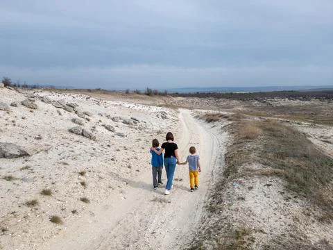 A mother and two child exploring a rocky outdoor landscape. The terrain is ru Stock Photos