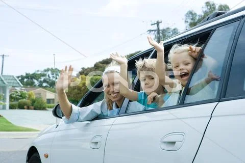 Mother And Two Children Waving Out Of Car Windows, Looking At Camera