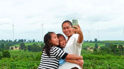 Mother and two daughters embracing and taking selfie with smartphone in wind far Video stock 342911030