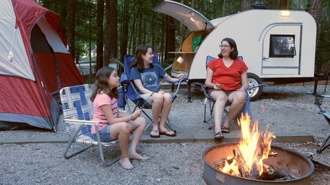 Mother and two daughters enjoying camping around a fire with teardrop camper. Video stock 108397341