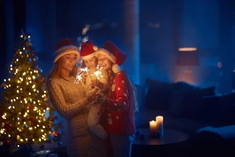 Mother and two daughters using sparklers near christmas tree Stock Photos