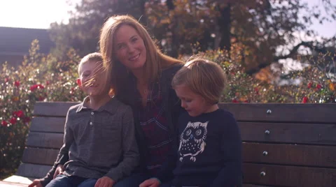 A mother and two kids posing for a picture on a bench at the park Stock Footage 61451553