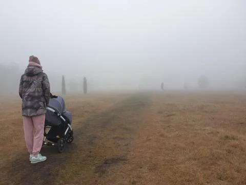 Mother with a baby carriage walks in a foggy park. Stock Photos