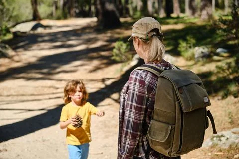 Mother with backpack receiving a pinecone from son in daylight Stock Photos