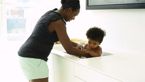 Mother bating infant sun in kitchen sink. 库存影片 89052215