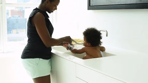 Mother bating infant sun in kitchen sink. Stock Footage 89052627