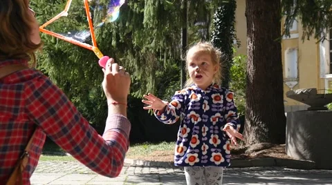 Mother blow big colored soap bubbles and child daughter jump chase burst them Stock Footage