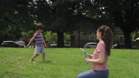 Mother blows bubbles for her son while he catches them in a park on a summer day Video stock 143622470