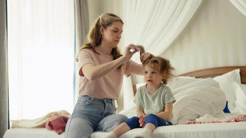 Mother brushing crying daughter's tangled hair in bedroom Stock Photos