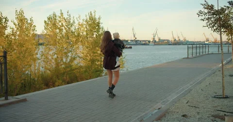 Mother carrying child while walking along riverside promenade Stock Footage 324704527