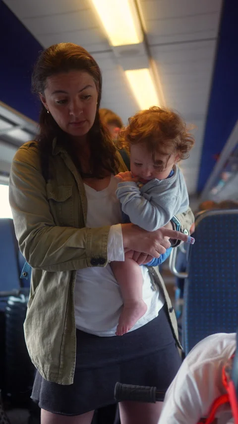 Mother carrying toddler while assisting older son on passenger train, highl.. Stock Footage 338133163