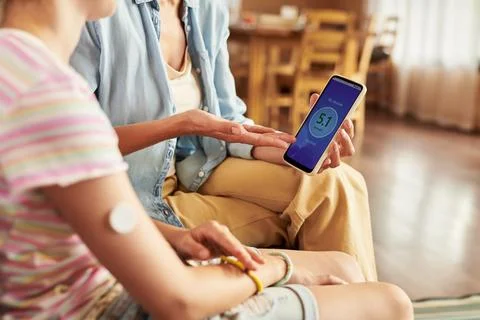 Mother Checking Blood Glucose Level on Smartphone with Daughter Stock Photos
