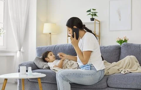 Mother checking temperature of child while calling doctor for consultation Foto stock