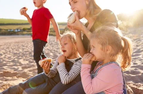 Mother With Children Eating Hot Dogs Sitting On Sand At Beach Barbecue Stock Photos