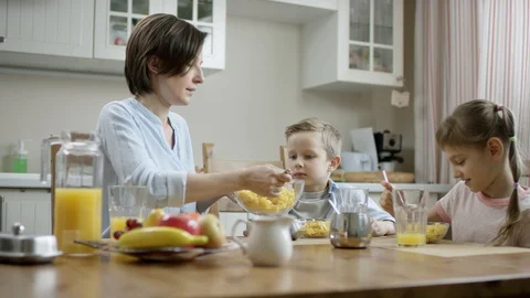 Mother communicate during breakfast with her children and put cornflakes from Stock Footage 107762817