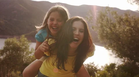 Mother with daughter on back, playing overlooking lake in countryside. Stock Footage 43670128