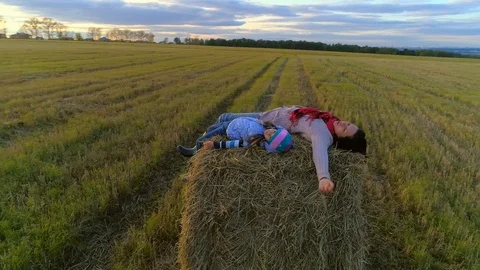 Mother with daughter lie on the straw stack on the rustic field in the sunset. Stock Footage 85667214