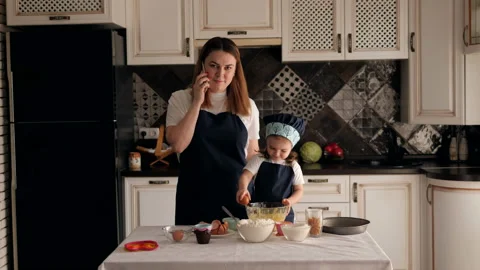 A mother with a daughter is preparing dough, mother is talking on the phone. Video stock 129383853