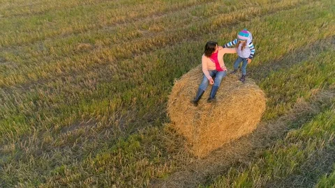 Mother with daughter sit on the straw stack on the rustic field in the sunset. Stock Footage 85667087