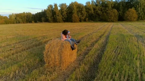 Mother with daughter sit on the straw stack on the rustic field in the sunset. Stock Footage 85667398