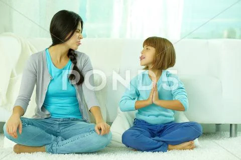Mother with daughter sitting in lotus position and showing tongue to each other Stock Photos