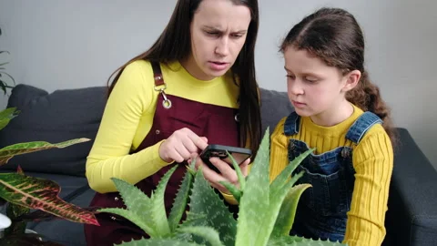 Mother with daughter using smartphone, reading information about plant diseases Stock Footage 234429204