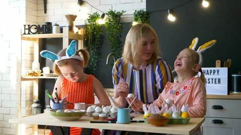 Mother is decorating Easter eggs with her daughters at home indoors. Video stock 151227700