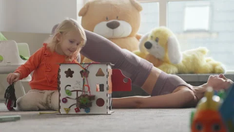 Mother does sport exercises while daughter plays at nursury room, glute bridge Video stock 230975043