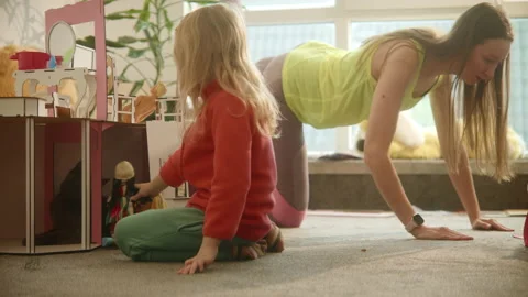 Mother does sport exercises while daughter plays at nursury room, workout Stock Footage 233961754