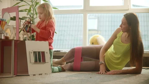 Mother does sport exercises while daughter plays with dolls toy house, nursury Stock Footage 234993365