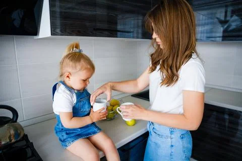 Mother is drinking tea in the kitchen with her little daughter. Stock Photos