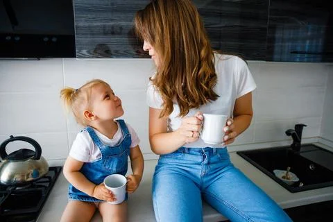 Mother is drinking tea in the kitchen with her little daughter. Stock Photos