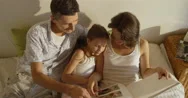 Mother, Father And Daughter Wearing Pajamas Reading A Book Together Laying  Stock Footage