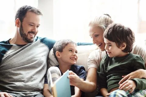 Mother, father and kids on sofa for storytelling time in living room of happy Stock Photos