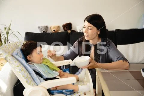 Mother feeding her baby son porridge in the child seat - Asian mixed ethnicity Stock Photos