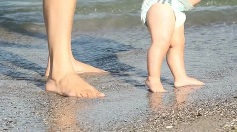 Mother feet and baby feet learning to walk at the beach Stock Footage