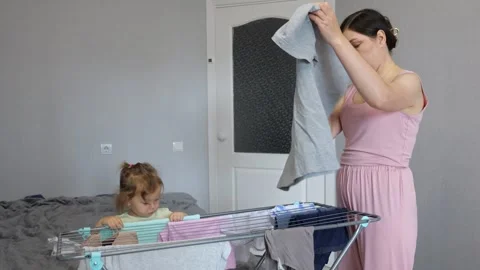 Mother folding laundry while daughter playing Stock Footage 303880119