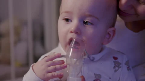 Mother gently administering inhalation therapy to baby at home, showcasing Video stock 323234522