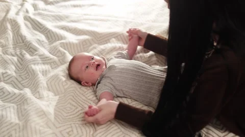Mother gently brushing her baby's hair on a patterned bed with soft natural Vidéo 340636970