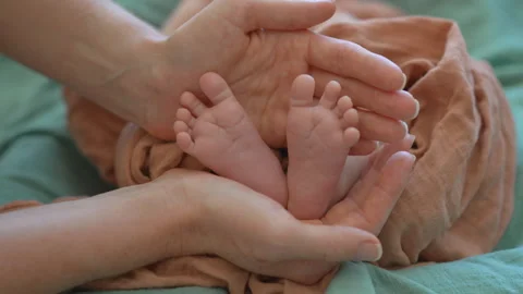 A mother gently cradles the tiny legs of her newborn baby in her hands Stock Footage 297478954
