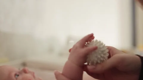 Mother gently massaging baby's tiny hand with a spiky sensory ball for Stock Footage 340630050