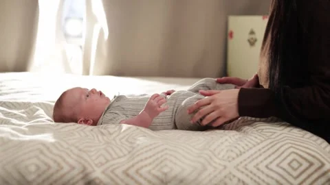 Mother gently touching her newborn baby lying on a bed with soft natural light Stockbeeldmateriaal 340636955