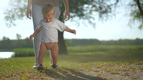 Mother guides son first steps on grass. Baby boy learning to walk outside with Stock-Footage 315901278