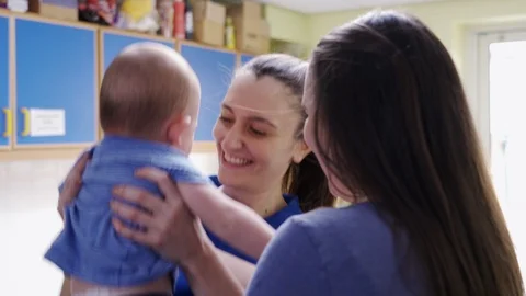 Mother Handing Baby Son To Female Nursery Worker At Childcare Centre Stock Footage
