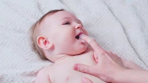 Mother hands brushing teeth with a finger brush of a happy infant baby. Mom doin Stock Footage 174871992
