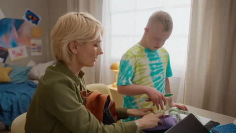 Mother Helping Boy with Down Syndrome Packing Backpack for School Stock Footage 337568358