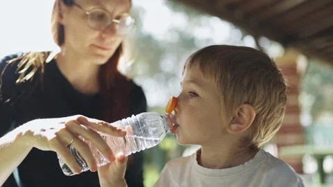 Mother helping child drinking water from plastic bottle at picnic Stock Footage 308008980